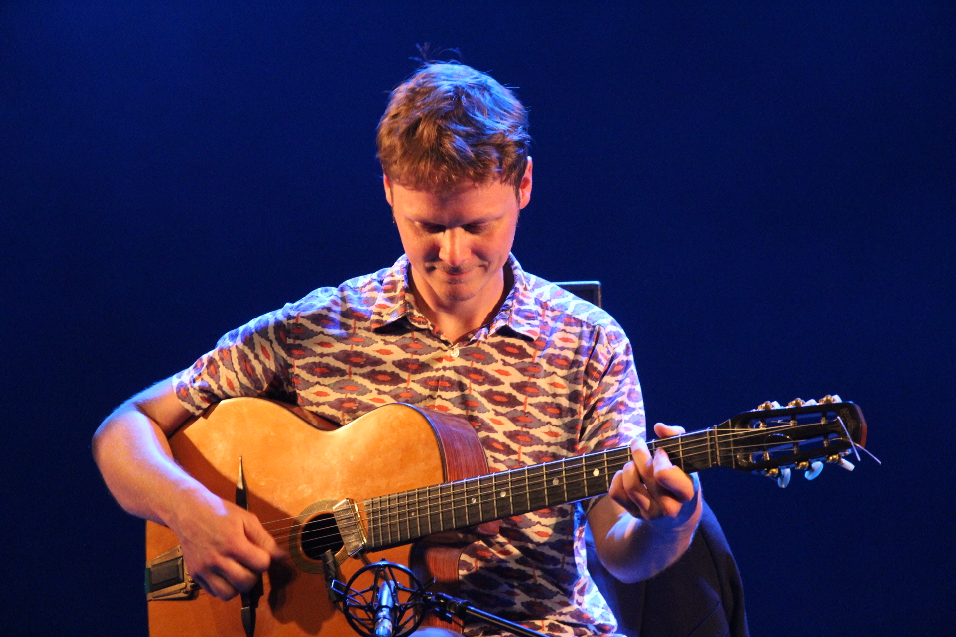 Jean Guyomarc’h playing guitar on stage under blue and amber lights